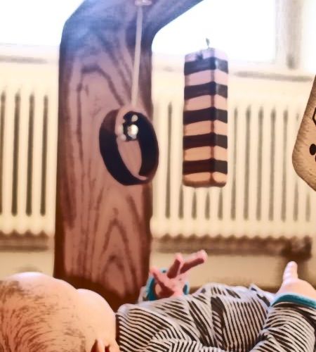 A baby is playing under baby toys made of wood.