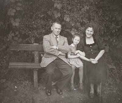A family is sitting on an old bench which stands in the neighbor's garden.