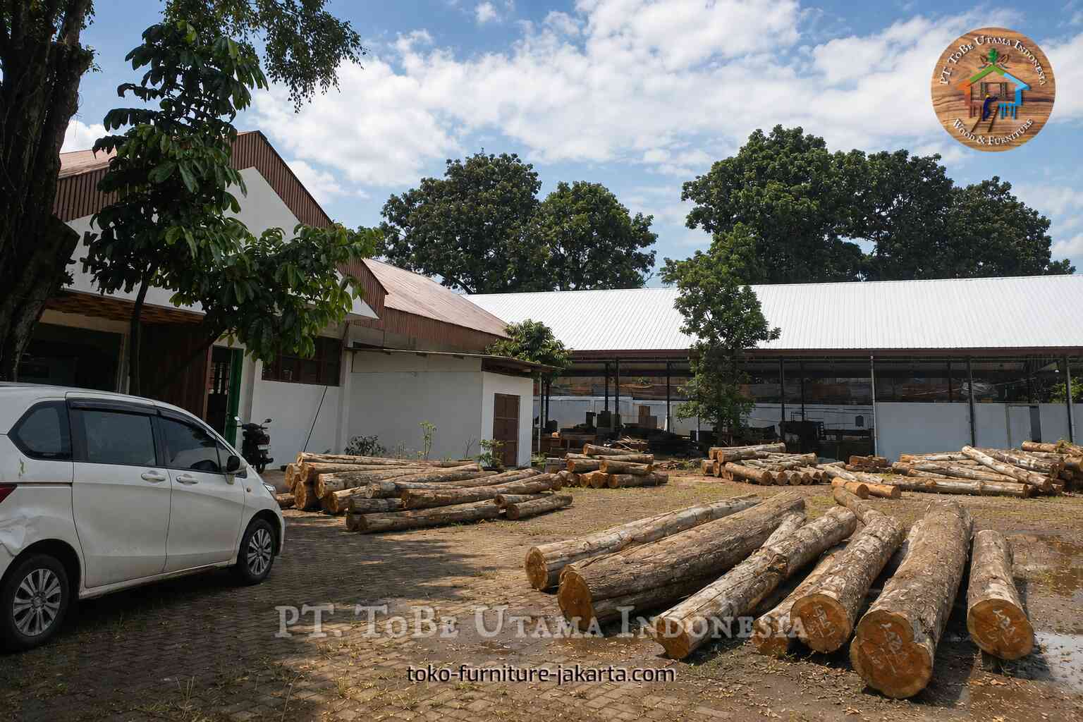 Tumpukan kayu gelondongan mentah tersebar di halaman pabrik.