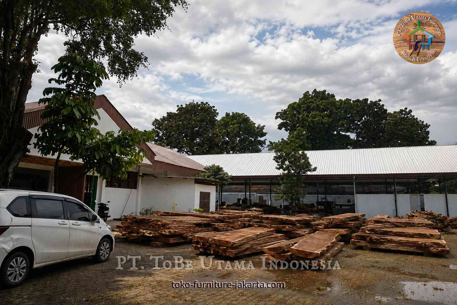 Tumpukan lempengan kayu tidak beraturan di halaman pabrik.